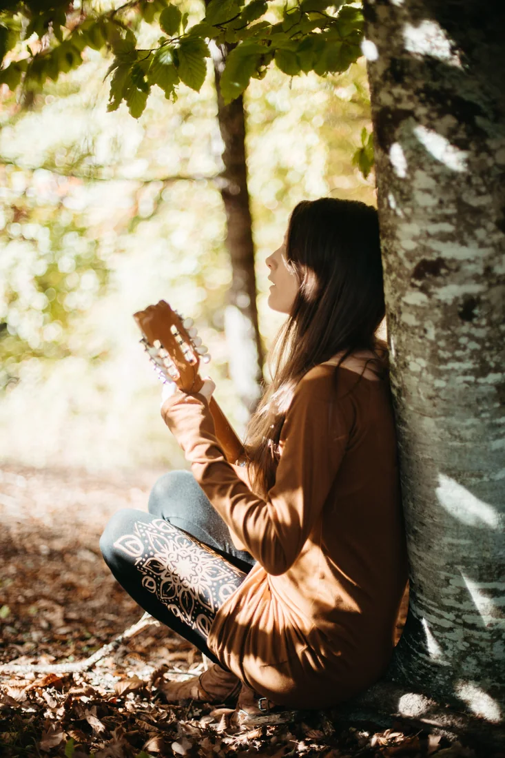 Floriane joue de la musique au pied d’un arbre.